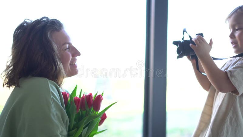 Een jongetje wenst zijn moeder een gelukkige verjaardag. een kind fotografeert zijn moeder met een bouquet tulpen in haar handen