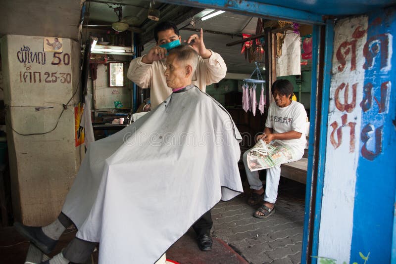 Een kapper snijdt het haar van zijn cliënt in een oude kapper in de straten van Bangkok royalty-vrije stock foto Een kapper snijdt het haar van zijn cliënt in een oude kapper in de straten van Bangkok royalty-vrije stock foto