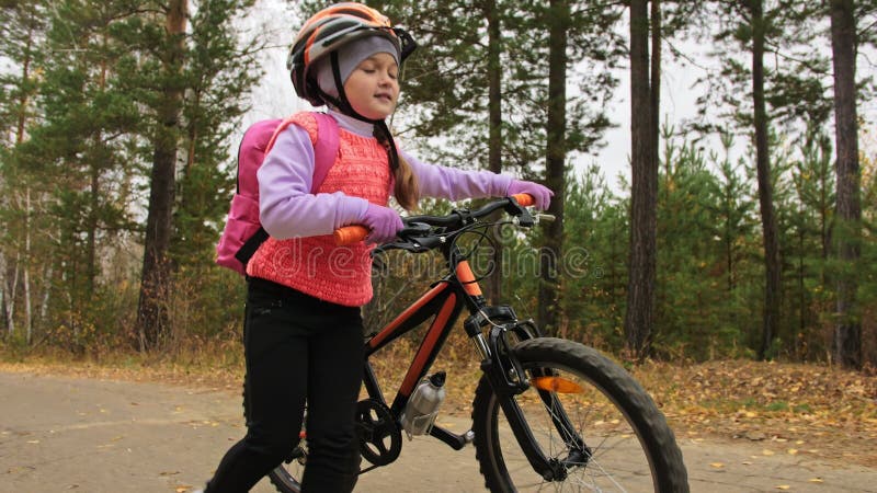 Een kaukasus kind wandelt met de fiets in het herfstpark Klein meisje met zwarte oranje cyclus in het bos Kid doet het wel