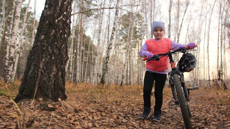 Een kaukasus kind wandelt met de fiets in het herfstpark Klein meisje met zwarte oranje cyclus in het bos Kid doet het wel