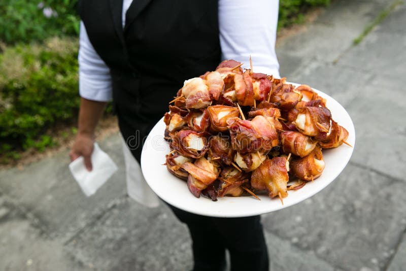 Een kelner die een plaathoogtepunt van bacon houden verpakte kammosselen - de reeks van de huwelijkscatering royalty-vrije stock foto Een kelner die een plaathoogtepunt van bacon houden verpakte kammosselen - de reeks van de huwelijkscatering royalty-vrije stock foto