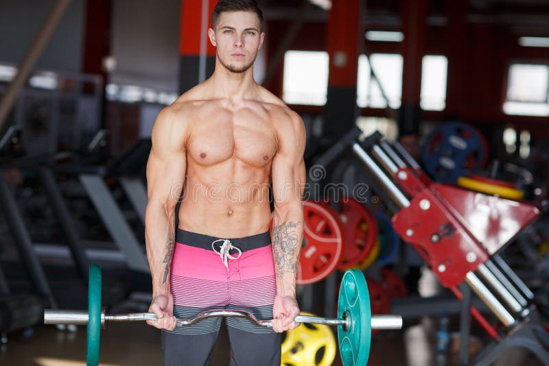 Een kerel met een w-Vormige bar met pannekoeken die oefeningen op een vage achtergrond van de gymnastiek doen stock foto Een kerel met een w-Vormige bar met pannekoeken die oefeningen op een vage achtergrond van de gymnastiek doen stock foto