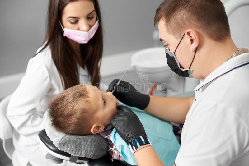 Een kind heeft zijn die tanden door een mannelijke tandarts die in een zwart masker en handschoenen worden bijgewoond door een mo stock foto's Een kind heeft zijn die tanden door een mannelijke tandarts die in een zwart masker en handschoenen worden bijgewoond door een mo stock foto's