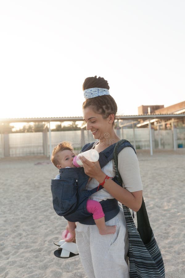 Een klein kind zit in een rugzak en loopt samen met de moeder langs de kust De vakantieconcept van de de zomerfamilie royalty-vrije stock foto Een klein kind zit in een rugzak en loopt samen met de moeder langs de kust De vakantieconcept van de de zomerfamilie royalty-vrije stock foto
