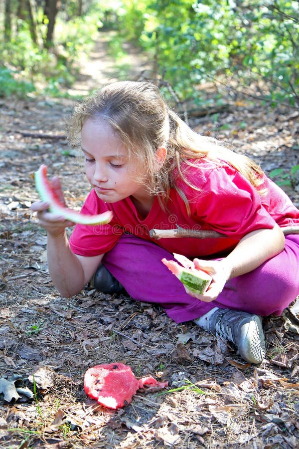 Een klein meisje in roze kleren eet watermeloenzitting op droog gras stock afbeeldingen Een klein meisje in roze kleren eet watermeloenzitting op droog gras stock afbeeldingen