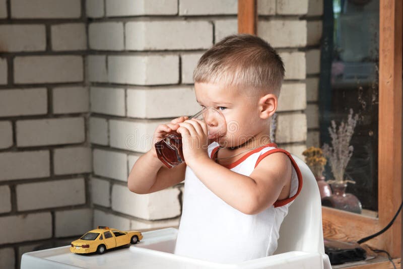 Een kleine jongen zit bij een lijst aangaande de veranda en drinkt compote stock afbeeldingen Een kleine jongen zit bij een lijst aangaande de veranda en drinkt compote stock afbeeldingen