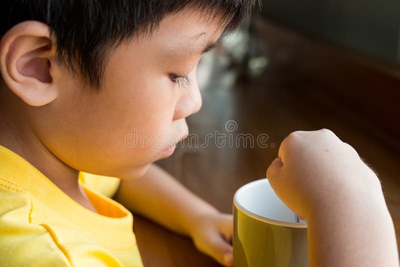 Een kleine jongenszitting bij de houten lijst door het venster thuis om een kop van hete chocolade te drinken hij houdt de kop in stock afbeeldingen Een kleine jongenszitting bij de houten lijst door het venster thuis om een kop van hete chocolade te drinken hij houdt de kop in stock afbeeldingen