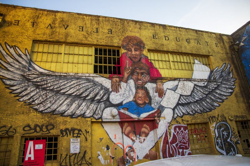 Een kleurrijke muurmuurmuurschildering met een jonge zwarte man met vleugels met een vrouw en een baby die in hoogte leest en onde