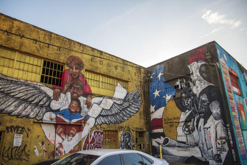 Een kleurrijke muurmuurschildering met een jonge zwarte man met vleugels met een vrouw en een baby die op hoogte is en onderwijst