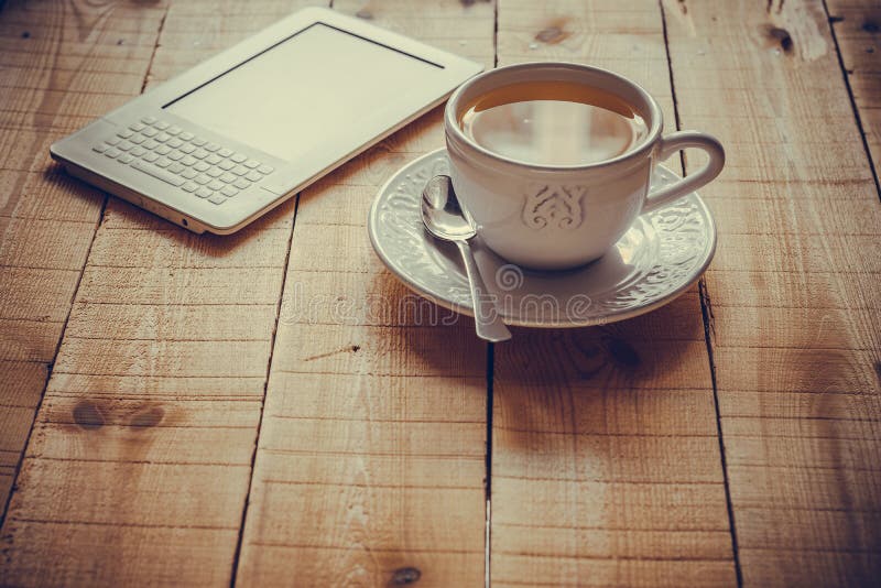Een kop thee en een ebooklezer op een houten lijst stock fotografie Een kop thee en een ebooklezer op een houten lijst stock fotografie