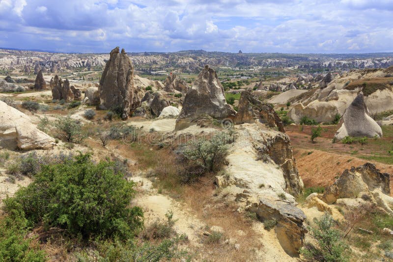 Een landweg kronkelt tussen kegelpieken van rotsen, oude holen binnen tegen de achtergrond van het berglandschap van de vallei stock foto's Een landweg kronkelt tussen kegelpieken van rotsen, oude holen binnen tegen de achtergrond van het berglandschap van de vallei stock foto's