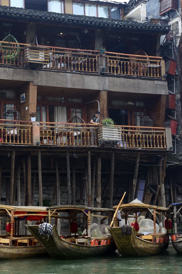 Een man in Fenghuang Ancient City zit op een balkon op een rij reisboten in de Tuo Jiang rivier hieronder royalty-vrije stock afbeelding Een man in Fenghuang Ancient City zit op een balkon op een rij reisboten in de Tuo Jiang rivier hieronder royalty-vrije stock afbeelding