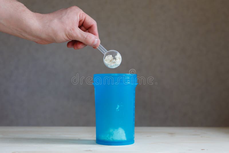 Een man hand houdt een lepel van weiproteïne en giet het in een schudbeker Sportendrank voor een reeks van zuivere spiermassa Cas stock foto Een man hand houdt een lepel van weiproteïne en giet het in een schudbeker Sportendrank voor een reeks van zuivere spiermassa Cas stock foto