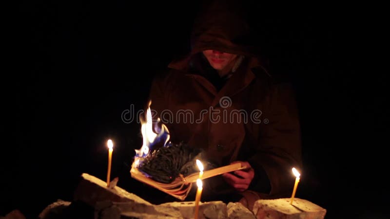 Een man met een kap leest een warm boek met kaarsen op de vloer