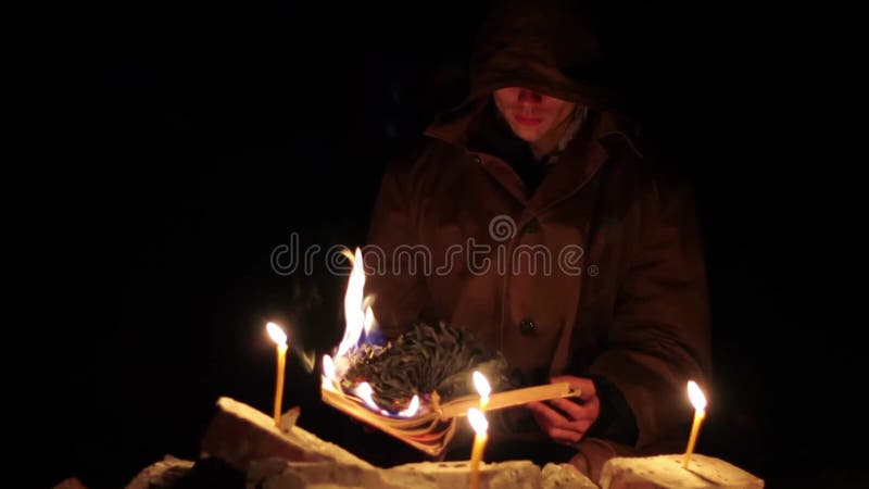 Een man met een kap leest een warm boek met kaarsen op de vloer