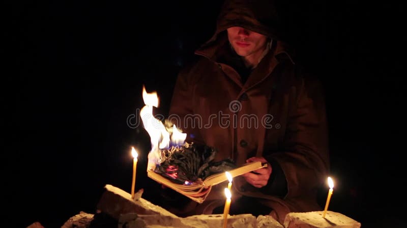 Een man met een kap leest een warm boek met kaarsen op de vloer