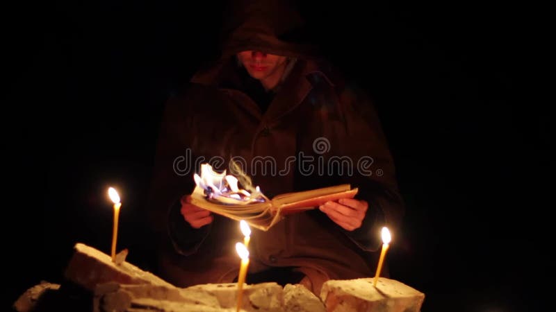 Een man met een kap leest een warm boek met kaarsen op de vloer