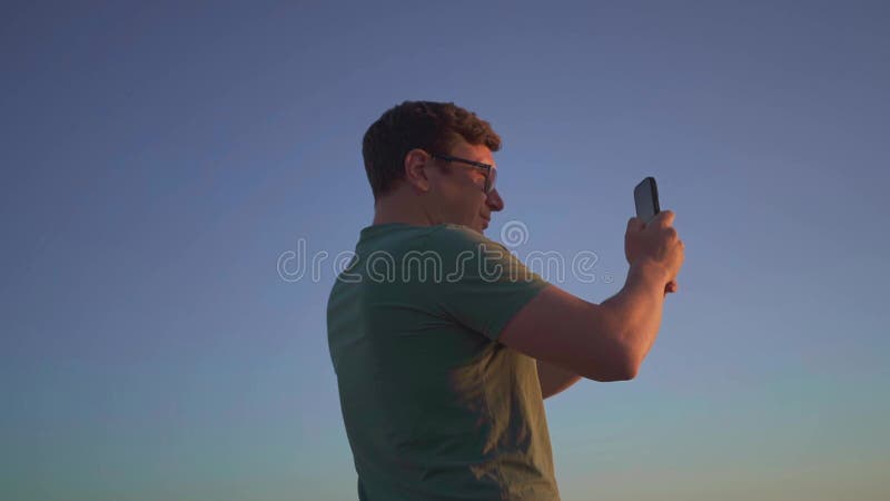 Een man met een sportieve band die zijn smartphone gebruikt om een serene zonsondergang te fotograferen die het moment vangt