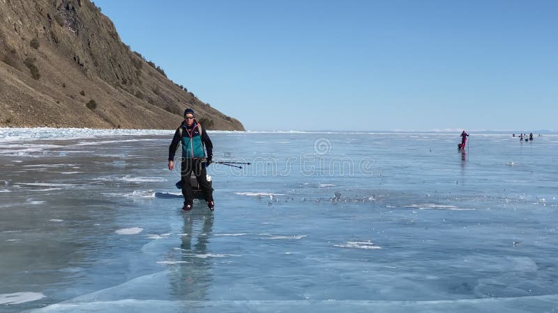 Een man op schaatsen zwaait zijn hand naar de camera. een groep toeristen reist op ijs op het ijs van het diepgevroren meer baikal