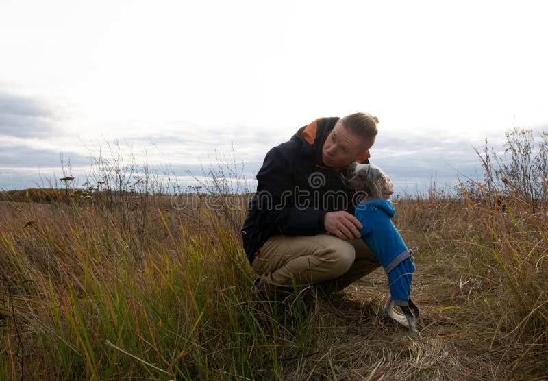 Een man van middelbare leeftijd loopt met een hondenras Chinees Hairless Crested Dog op de natuur in de herfstnamiddag stock afbeelding Een man van middelbare leeftijd loopt met een hondenras Chinees Hairless Crested Dog op de natuur in de herfstnamiddag stock afbeelding