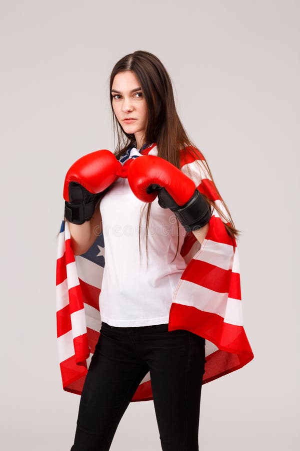 Een meisje die terwijl status in bokshandschoenen en behandeld met een Amerikaanse vlag stellen royalty-vrije stock afbeelding Een meisje die terwijl status in bokshandschoenen en behandeld met een Amerikaanse vlag stellen royalty-vrije stock afbeelding