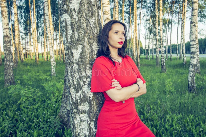 Een meisje met rode lippen in een rode kleding bevindt zich in een de modestijl van het berkbosje royalty-vrije stock foto Een meisje met rode lippen in een rode kleding bevindt zich in een de modestijl van het berkbosje royalty-vrije stock foto