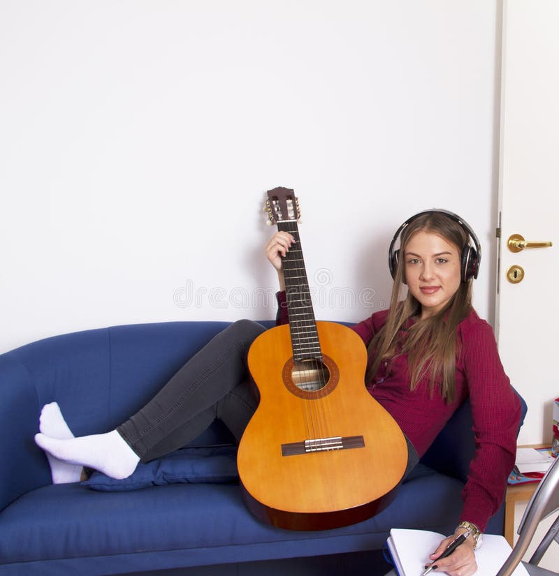 Een meisje in een rood overhemd houdt een gitaar en luistert aan muziek en schrijft een lied in een notaboek stock afbeelding Een meisje in een rood overhemd houdt een gitaar en luistert aan muziek en schrijft een lied in een notaboek stock afbeelding