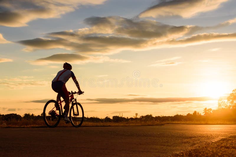Een mens berijdt een fiets bij zonsondergang met zonnestraal stock afbeelding Een mens berijdt een fiets bij zonsondergang met zonnestraal stock afbeelding
