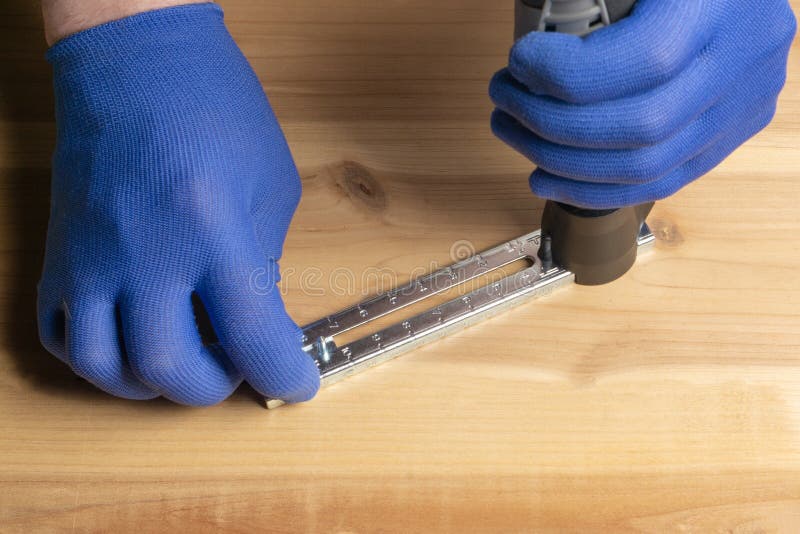 Een mens in blauwe handschoenen snijdt een gat in een blad van triplex stock foto Een mens in blauwe handschoenen snijdt een gat in een blad van triplex stock foto