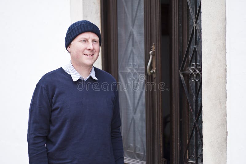 Een mens die zich naast bruine hoofddeur aan wit huis bevinden royalty-vrije stock foto Een mens die zich naast bruine hoofddeur aan wit huis bevinden royalty-vrije stock foto