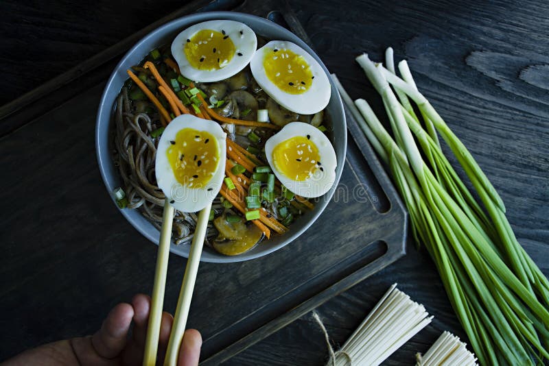 Een mens eet de noedels van boekweitsoba met saus en bijgerechten in bouillon Japans voedsel Aziatische keuken Zwarte houten acht stock afbeelding Een mens eet de noedels van boekweitsoba met saus en bijgerechten in bouillon Japans voedsel Aziatische keuken Zwarte houten acht stock afbeelding