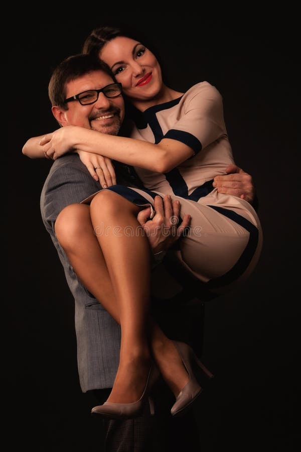 Een mens houdt een meisje in zijn wapens op een donkere achtergrond stock fotografie Een mens houdt een meisje in zijn wapens op een donkere achtergrond stock fotografie