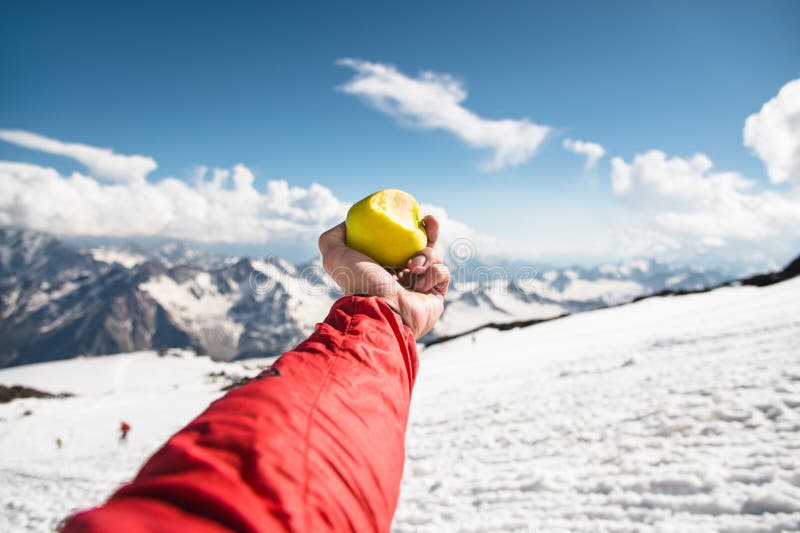 Een mensen` s hand houdt een appel met een beet op de achtergrond van snow-covered underfoot bergen en sneeuw stock fotografie Een mensen` s hand houdt een appel met een beet op de achtergrond van snow-covered underfoot bergen en sneeuw stock fotografie