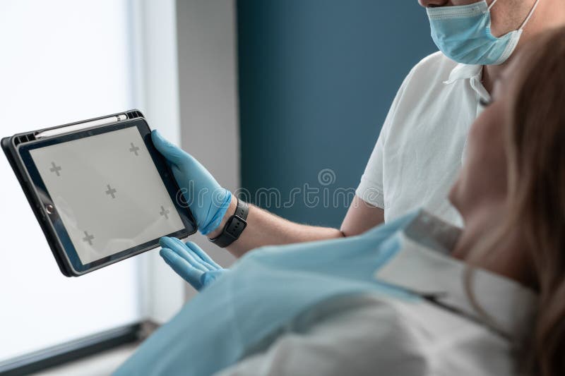 In a modern dental office, a dentist confidently demonstrates information to the patient on a tablet, providing clear explanations and recommendations. Template to insert. High quality photo. In a modern dental office, a dentist confidently demonstrates information to the patient on a tablet, providing clear explanations and recommendations. Template to insert. High quality photo