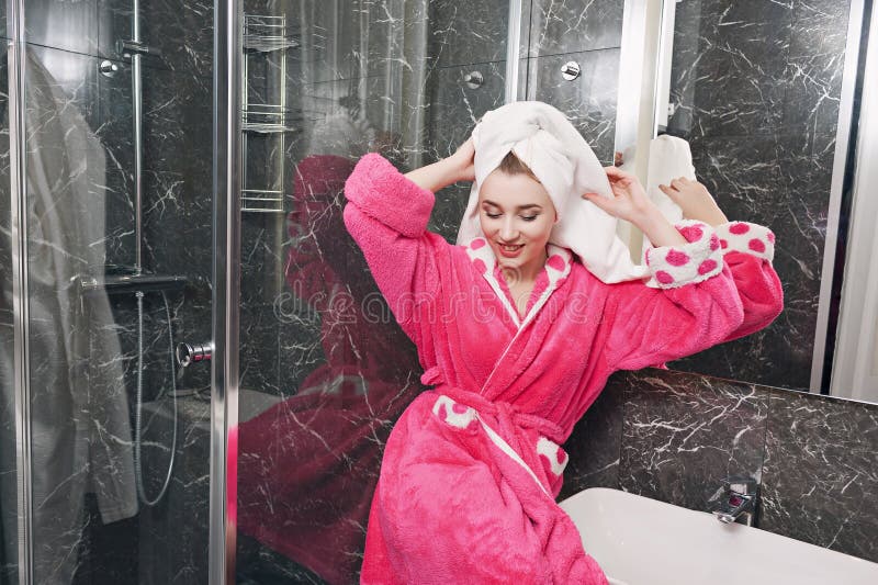 Een mooi jong meisje in een roze peignoir en een witte handdoek op haar hoofd, na een douche Wellness en kuuroordconcept stock afbeeldingen Een mooi jong meisje in een roze peignoir en een witte handdoek op haar hoofd, na een douche Wellness en kuuroordconcept stock afbeeldingen