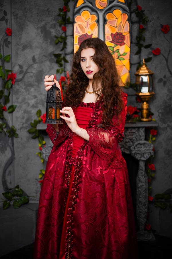 Een Mooi Meisje in Een Prachtige Rode Jurk Van Het Rococo Tijdperk Staat Tegen Een Haard in Raam En Bloemen Met Een Lamp Met Stock Afbeelding - Image of eeuw,