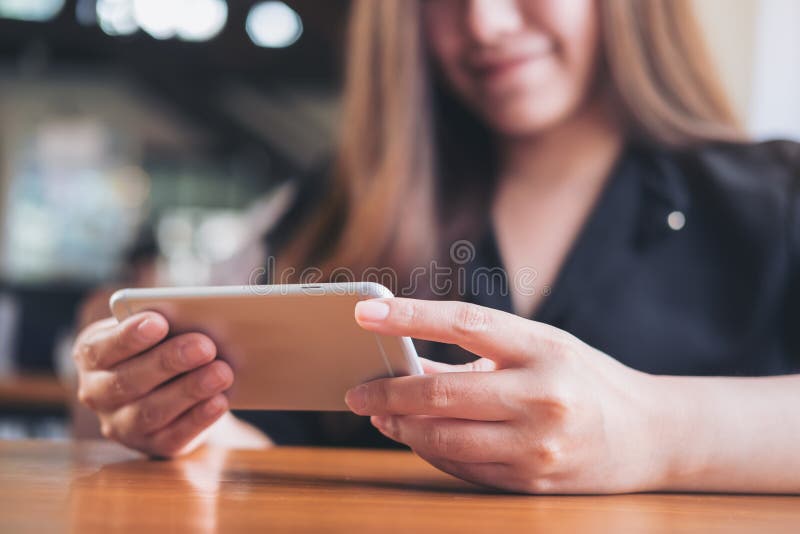 Een mooie Aziatische vrouw met smileygezicht die en horizontale slimme telefoon houden met behulp van aan het letten op TV en het stock afbeelding Een mooie Aziatische vrouw met smileygezicht die en horizontale slimme telefoon houden met behulp van aan het letten op TV en het stock afbeelding
