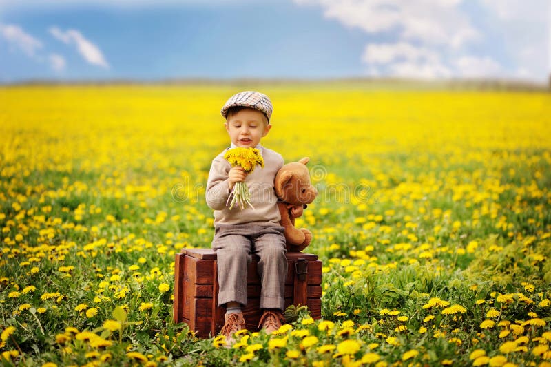 Een mooie, het glimlachen jongenszitting op de doos met teddybeer bij de lente Hazel boom royalty-vrije stock afbeelding Een mooie, het glimlachen jongenszitting op de doos met teddybeer bij de lente Hazel boom royalty-vrije stock afbeelding