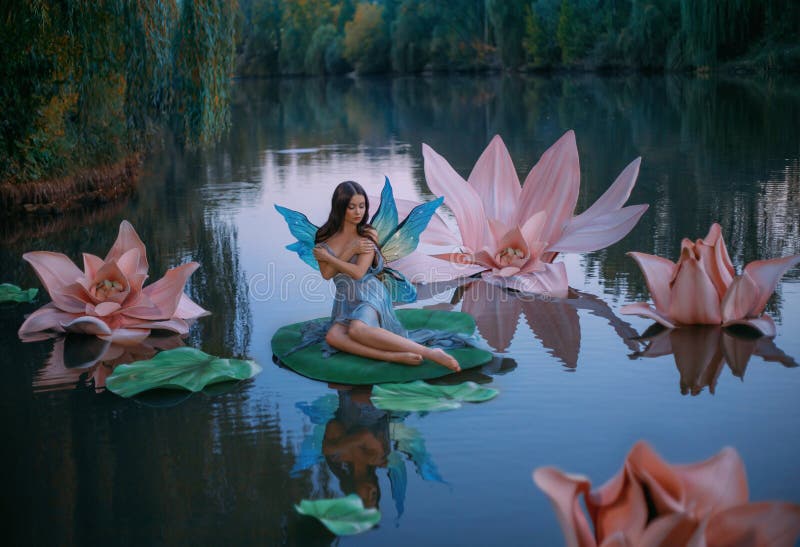 Een mooie vrouw met vlindervleugels zit op het blad van de groene waterlelui .. fantasiegebied van enorme