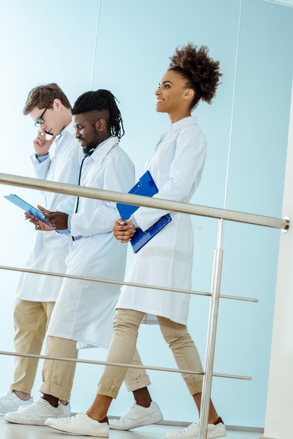 Een multiraciale groep medische internen die onderaan de de holding van de het ziekenhuisgang klemborden en het spreken lopen royalty-vrije stock foto's Een multiraciale groep medische internen die onderaan de de holding van de het ziekenhuisgang klemborden en het spreken lopen royalty-vrije stock foto's