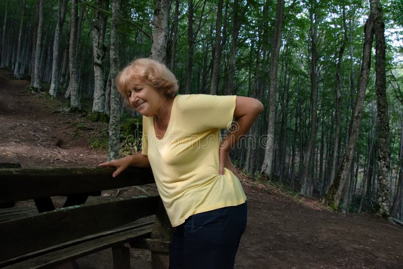 Een oudere vrouw geeft rugpijn. een trieste blonde vrouw met middelbare leeftijd , die na een oorlog pijn in de rug in het bos ond