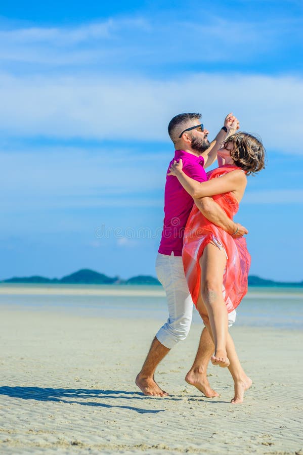 Een paar die pret op strand hebben Witte t-shirt, witte broeken en zonnebril Witte bikini, blootvoets op wit zand royalty-vrije stock afbeeldingen Een paar die pret op strand hebben Witte t-shirt, witte broeken en zonnebril Witte bikini, blootvoets op wit zand royalty-vrije stock afbeeldingen