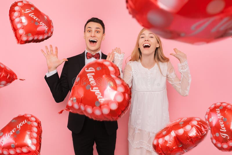 Een paar in liefde, een man en een vrouw, die ballons in de vorm van een hart op een roze achtergrond houden, genieten van de dag royalty-vrije stock foto's Een paar in liefde, een man en een vrouw, die ballons in de vorm van een hart op een roze achtergrond houden, genieten van de dag royalty-vrije stock foto's
