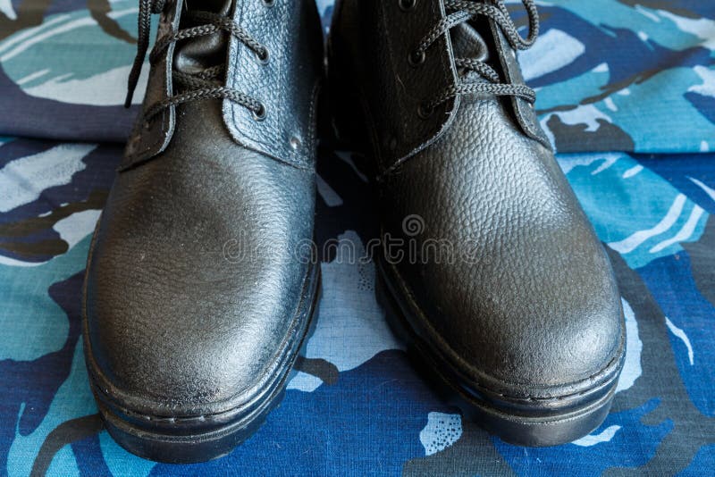 Een paar zwarte legerlaarzen op stof met blauwe camouflage Geen mensen Legerlaarzen voor de militair Het voordeel van de Schoen stock foto's Een paar zwarte legerlaarzen op stof met blauwe camouflage Geen mensen Legerlaarzen voor de militair Het voordeel van de Schoen stock foto's