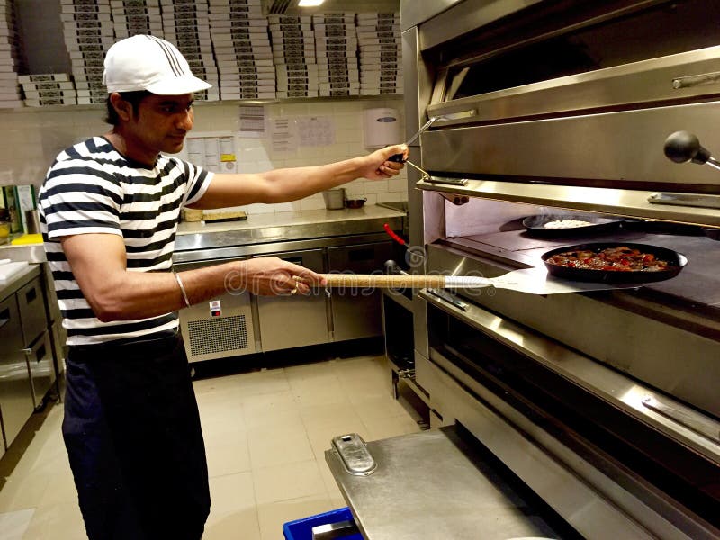 Een Pizzaiolo die een pizza van een steenoven terugtrekken stock afbeelding Een Pizzaiolo die een pizza van een steenoven terugtrekken stock afbeelding