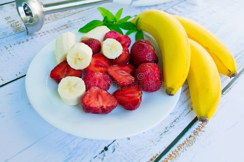 Een plaat met aardbeien en een banaan en een mixer op een witte houten lijst royalty-vrije stock foto Een plaat met aardbeien en een banaan en een mixer op een witte houten lijst royalty-vrije stock foto