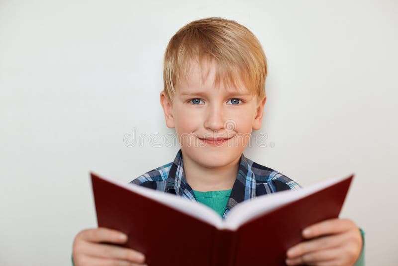 Een portret van knap weinig jongen die met eerlijk haar en blauwe ogen een boek in zijn handen houden terwijl status over witte a royalty-vrije stock foto's Een portret van knap weinig jongen die met eerlijk haar en blauwe ogen een boek in zijn handen houden terwijl status over witte a royalty-vrije stock foto's