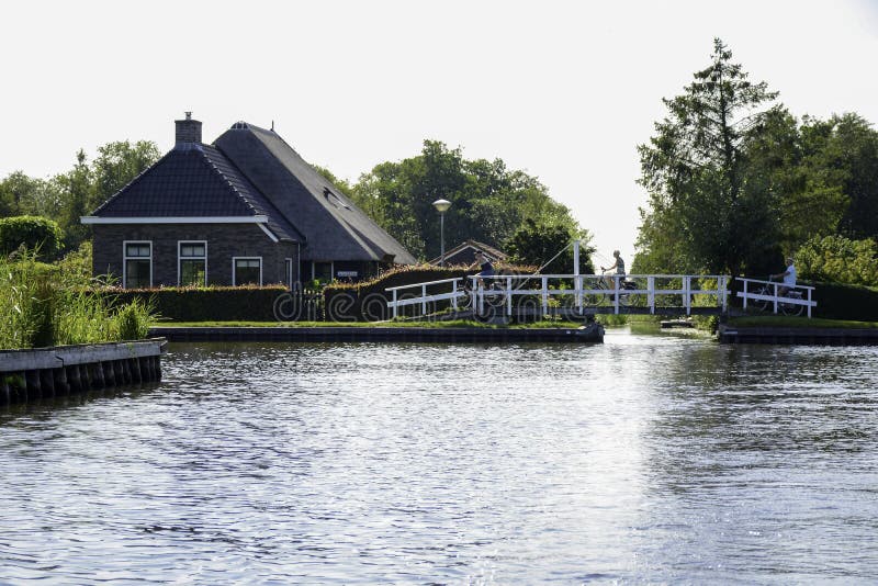 Een prachtig landschap tijdens de zomer met een kleine brug en fietstoeristen en met een typisch nederlands huis naast het kanaal stock afbeelding Een prachtig landschap tijdens de zomer met een kleine brug en fietstoeristen en met een typisch nederlands huis naast het kanaal stock afbeelding