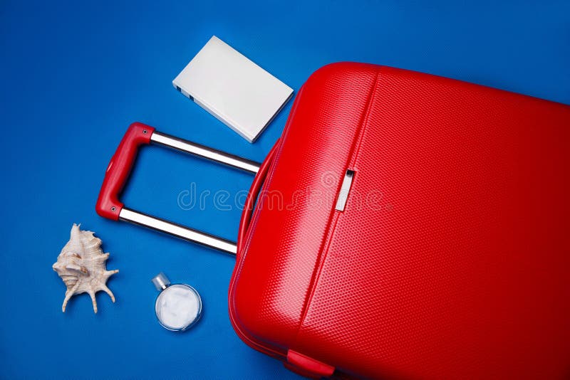 Een rode grote reiskoffer op wielen met een intrekbare handgreep, omringd door een parfumefles, naai en een wit blanco boek