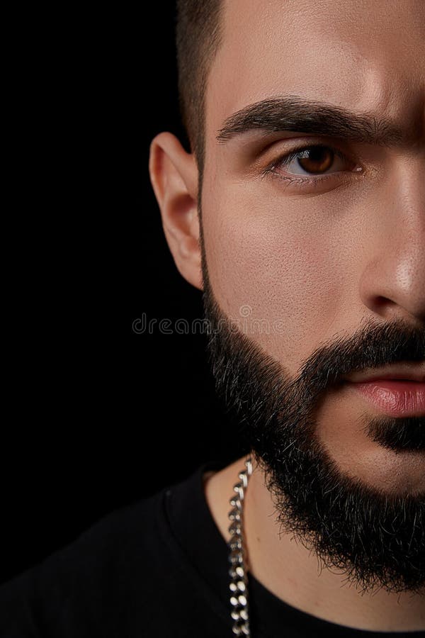 A close-up dramatic portrait of a young serious guy, musician, singer,rapper with a beard and arms crossed on his chest on a black isolated background. A close-up dramatic portrait of a young serious guy, musician, singer,rapper with a beard and arms crossed on his chest on a black isolated background.